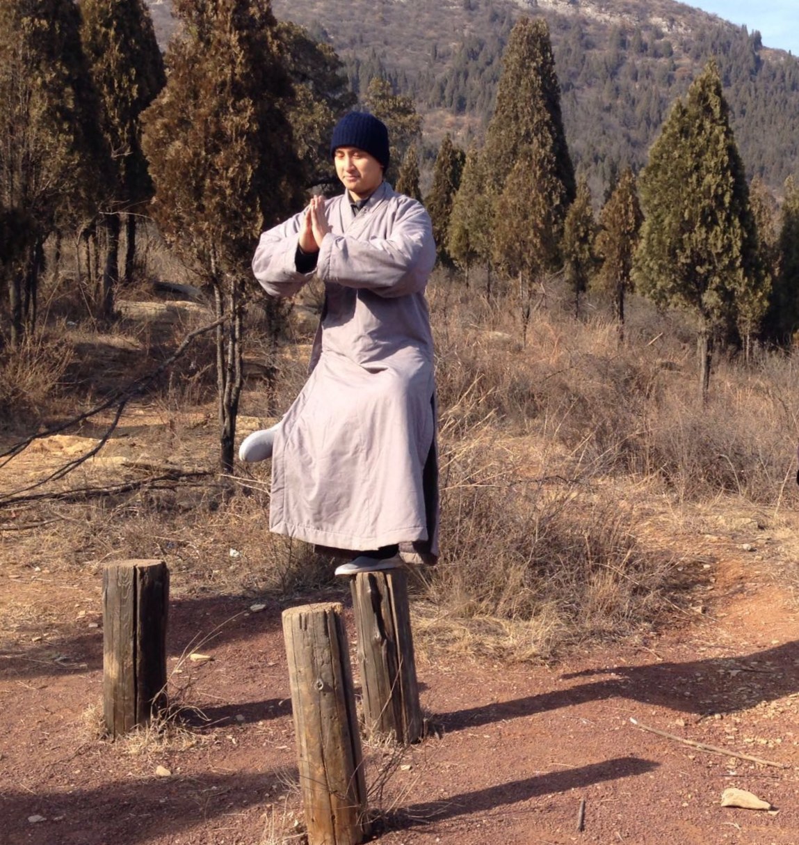 Master Peter Wu practicing balance training standing on wooden stakes on Mount Song, China, hands pressed together